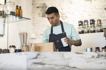 Man holding disposable coffee cup working in cafe - JCCMF06738