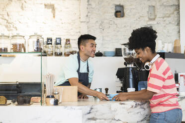 Lächelnder Mann, der einem Kunden in einem Café Kaffee serviert - JCCMF06740