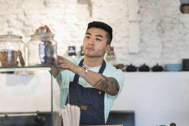 Young man wearing apron working in cafe - JCCMF06741