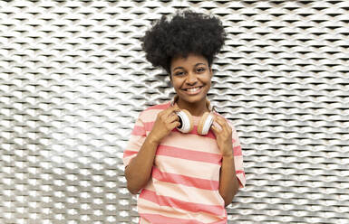 Lächelnde junge Frau mit Afrofrisur vor einer Wand stehend - JCCMF06761