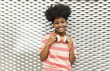 Smiling young woman with Afro hairstyle standing in front of wall - JCCMF06761