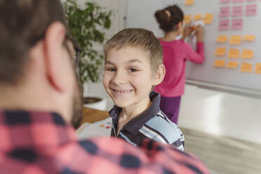 Lächelnder Junge neben einem Lehrer mit einer Schwester, die auf einer Tafel im Hintergrund schreibt - OSF00377