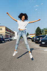 Happy woman with arms outstretched jumping on road - MEUF06929