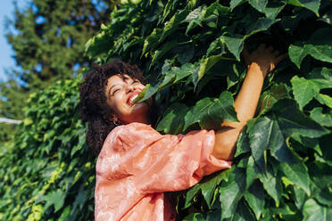 Happy woman embracing green leaves on sunny day - MEUF06947