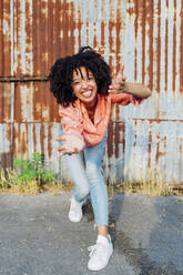 Cheerful young woman with curly hair gesturing on footpath - MEUF06959