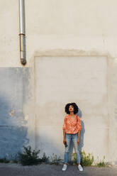 Woman with curly hair holding smart phone in front of wall - MEUF06963