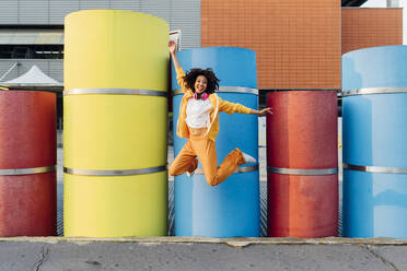 Happy woman jumping in front of colorful pipes - MEUF06977