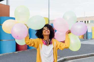 Glückliche Frau spielt mit bunten Luftballons auf dem Fußweg - MEUF06982