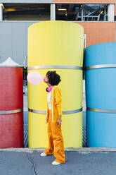 Woman blowing bubblegum in front of multi colored pipes - MEUF06995