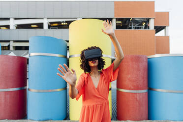 Junge Frau in einem Virtual-Reality-Simulator gestikuliert vor einem bunten Rohr - MEUF07018