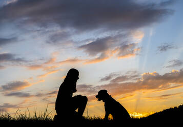 Silhouette der Frau spielt mit Hund gegen Wolken bei Sonnenuntergang - STSF03322