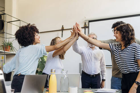 Cheerful business colleagues giving high-five to each other at office - MEUF07041