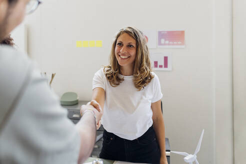 Lächelnde Geschäftsfrau beim Händeschütteln mit einem Kollegen im Büro - MEUF07059