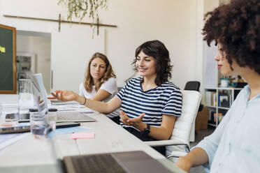 Smiling businesswoman gesturing in meeting by colleagues at office - MEUF07070