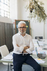 Businessman wearing eyeglasses with arms crossed at office - MEUF07088