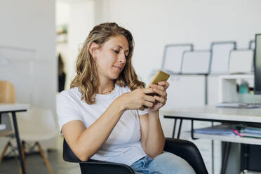 Businesswoman using smart phone sitting in office - MEUF07104