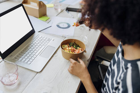 Businesswoman having poke bowl by laptop in lunch break at office - MEUF07121