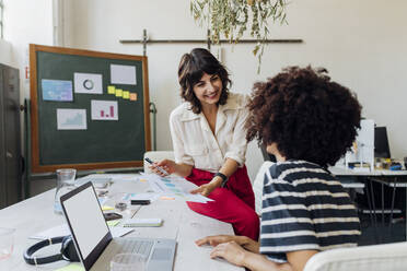 Smiling businesswoman explaining report to colleague at work place - MEUF07135