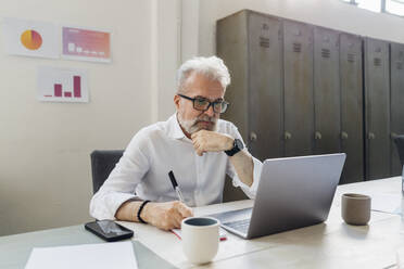Nachdenklicher Geschäftsmann mit Blick auf den Laptop im Büro - MEUF07139