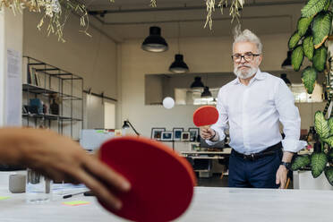 Geschäftsmann spielt Tischtennis mit einem Kollegen im Büro - MEUF07154