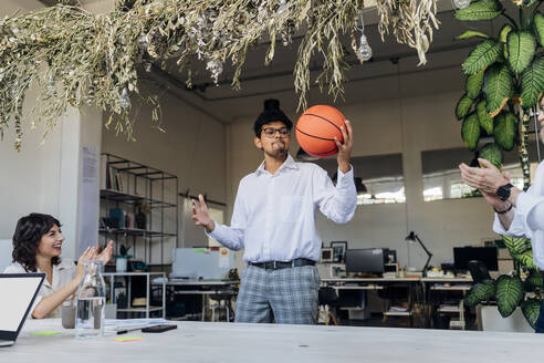 Geschäftsmann spielt Basketball mit jubelnden Kollegen im Büro - MEUF07155