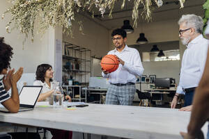 Geschäftsmann mit Basketball im Gespräch mit Kollegen im Büro - MEUF07156