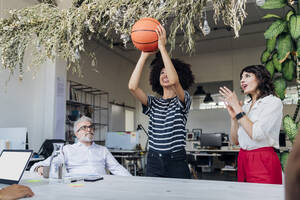 Geschäftsfrau spielt Basketball, während ein Kollege im Büro jubelt - MEUF07159