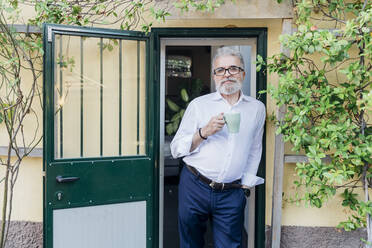 Geschäftsmann mit Kaffeetasse an der Tür lehnend - MEUF07168