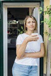 Selbstbewusste Geschäftsfrau mit Kaffeetasse an der Eingangstür - MEUF07173