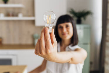 Woman holding light bulb at home - MEUF07204