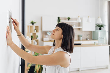 Woman using automation device on wall at home - MEUF07206