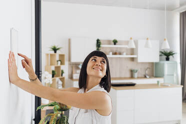 Woman operating home automation device on wall at home - MEUF07207