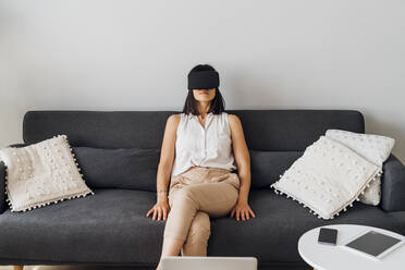 Frau mit Virtual-Reality-Brille sitzt zu Hause auf dem Sofa - MEUF07224