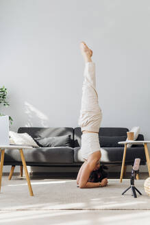 Frau macht Kopfstand im Online-Yoga-Kurs zu Hause - MEUF07269