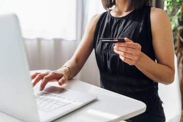 Woman holding credit card doing online shopping through laptop - MEUF07292