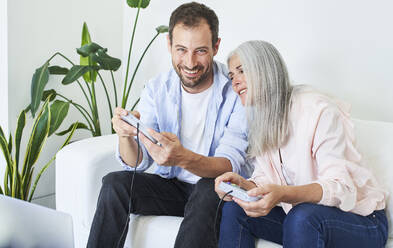 Glücklicher Mann mit Mutter, die ein Videospiel spielt, sitzt auf dem Sofa im Wohnzimmer zu Hause - VEGF05668