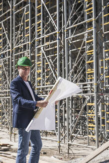 Lächelnder leitender Ingenieur mit Bauplan auf einer Baustelle - UUF26828