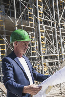 Ingenieur mit Schutzhelm bei der Analyse von Plänen auf der Baustelle - UUF26831