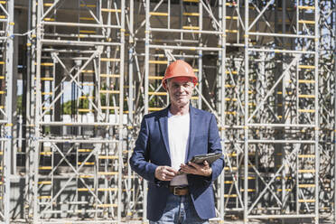 Smiling engineer with tablet PC standing in front of scaffolding - UUF26835