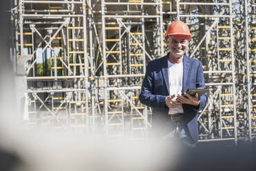 Smiling architect with tablet PC standing at construction site - UUF26836