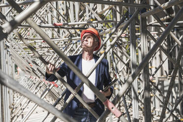 Engineer examining scaffolding at construction site on sunny day - UUF26841