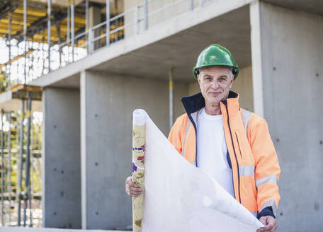 Lächelnder älterer Bauarbeiter mit Bauplan auf der Baustelle - UUF26843