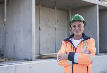 Smiling building contractor with arms crossed standing at construction site - UUF26850