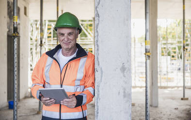 Lächelnder Bauunternehmer mit Tablet-PC, der an einer Säule lehnt - UUF26854