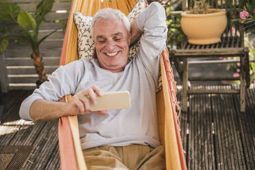 Glücklicher Mann im Ruhestand benutzt Telefon in der Hängematte - UUF26861