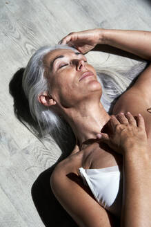 Mature woman with hand on chest lying under sunlight - VEGF05686