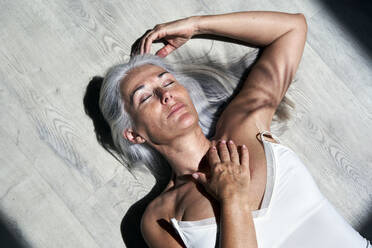 Mature woman with eyes closed and hand on chest resting under sunlight - VEGF05688