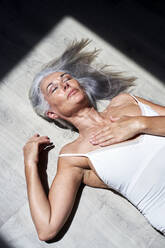 Mature woman with hand on chest resting under sunlight - VEGF05691