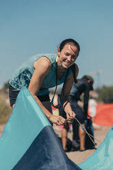 Lächelnde Frau beim Vorbereiten der Ausrüstung für das Kitesurfen am Strand - DMGF00803