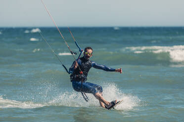 Mann im Neoprenanzug beim Kiteboarden im Meer an einem sonnigen Tag - DMGF00806